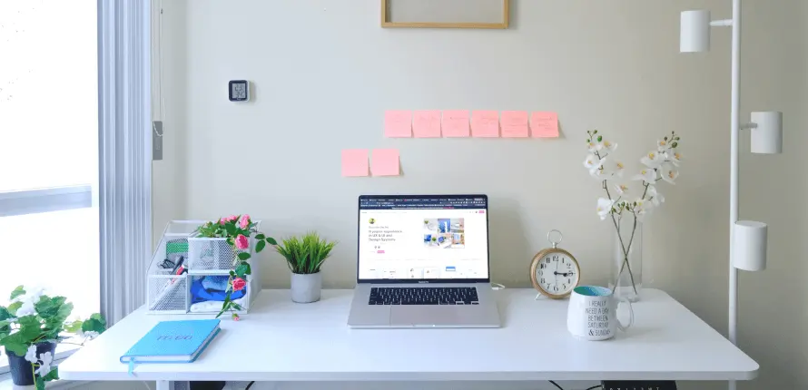 clean, minimalist workspace with a laptop, plants, a clock, sticky notes