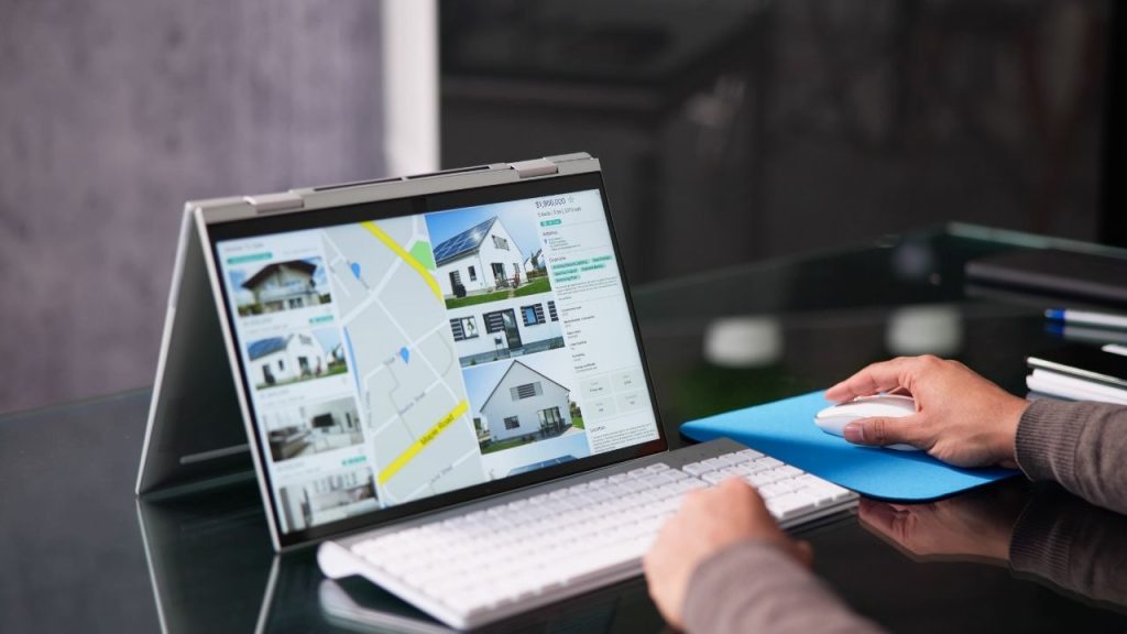 person using a laptop to browse real estate listings with property images.